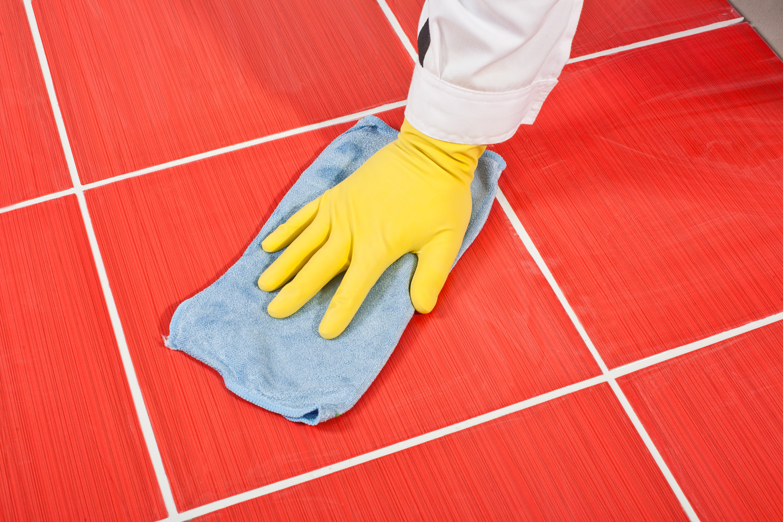 Worker with yellow gloves and blue towel clean red tiles grout
